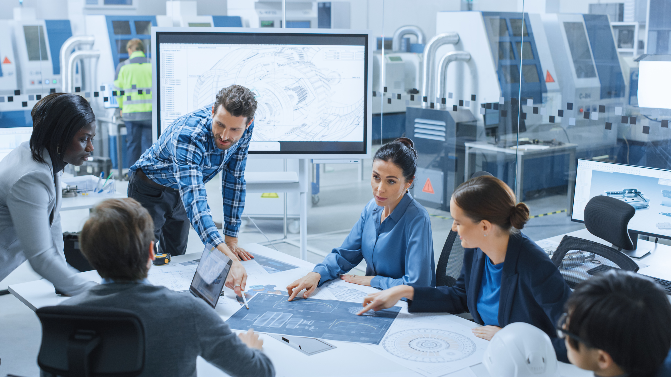 Six colleagues discussing work around a table in front of a whiteboard showing a chart.